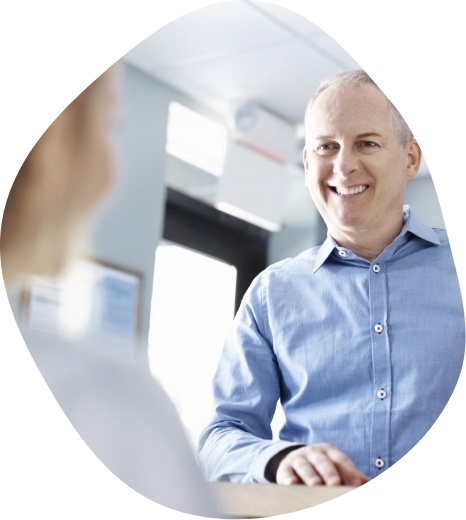 Man in light blue shirt smiling at person sitting at reception desk