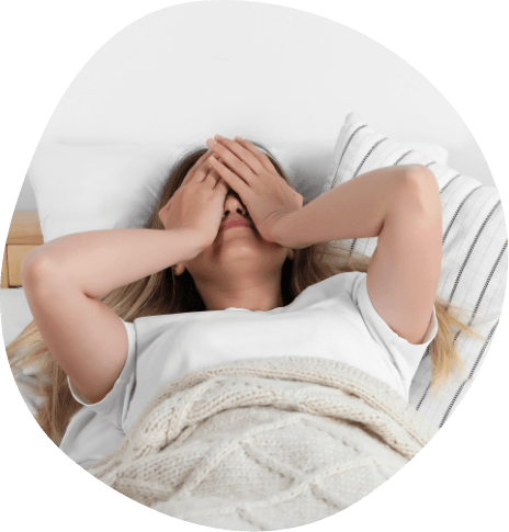 Woman lying in bed covering her face with her hands