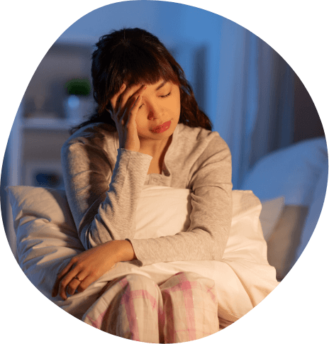 Woman sitting on edge of bed touching her temple in frustration