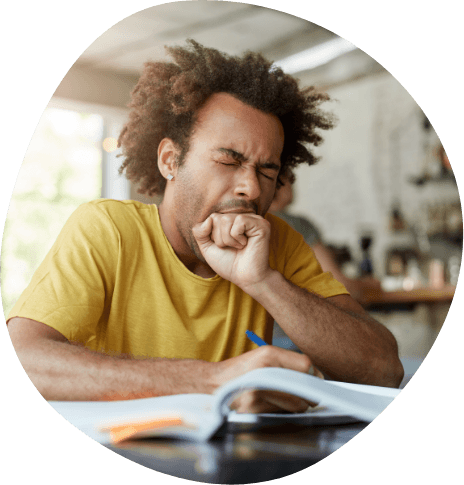 Man yawning while writing on paper at table