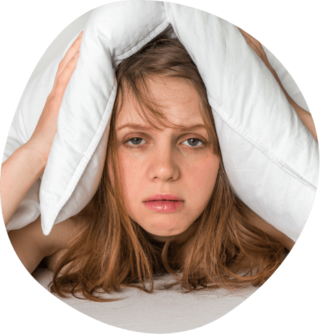 Woman lying in bed and covering the top of her head with a pillow