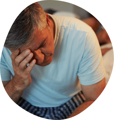 Older man sitting on edge of bed and touching forehead in frustration