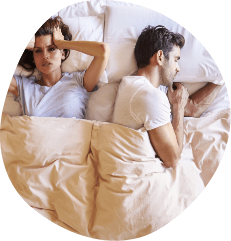 Woman in bed covering her ears next to snoring man