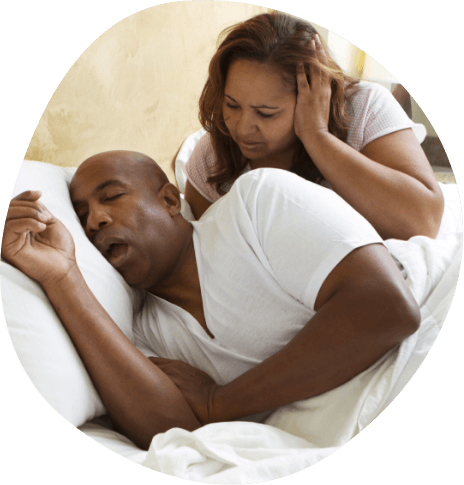 Woman in bed covering her ears while glaring at snoring man next to her