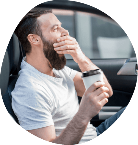 Man holding cup of coffee and yawning while driving
