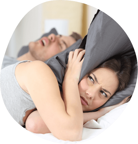 Woman covering her ears with pillow next to snoring man