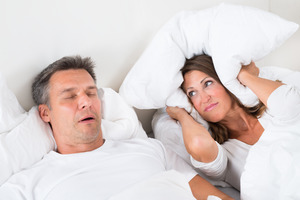 Man snoring in bed, woman covering ears with pillow