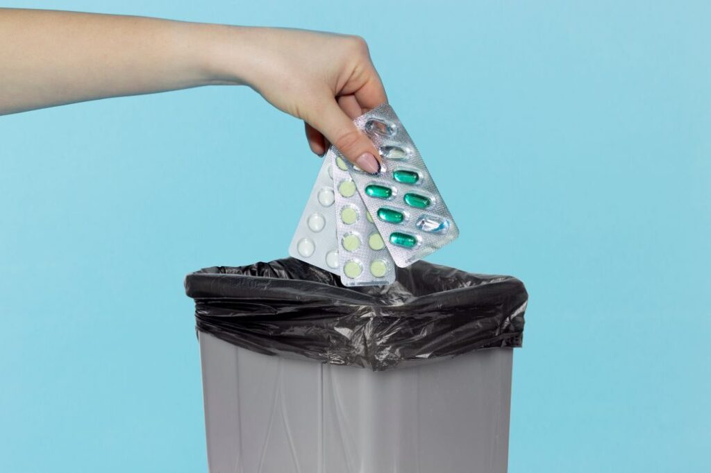 A woman’s hand throwing sleeping pills into a garbage can.